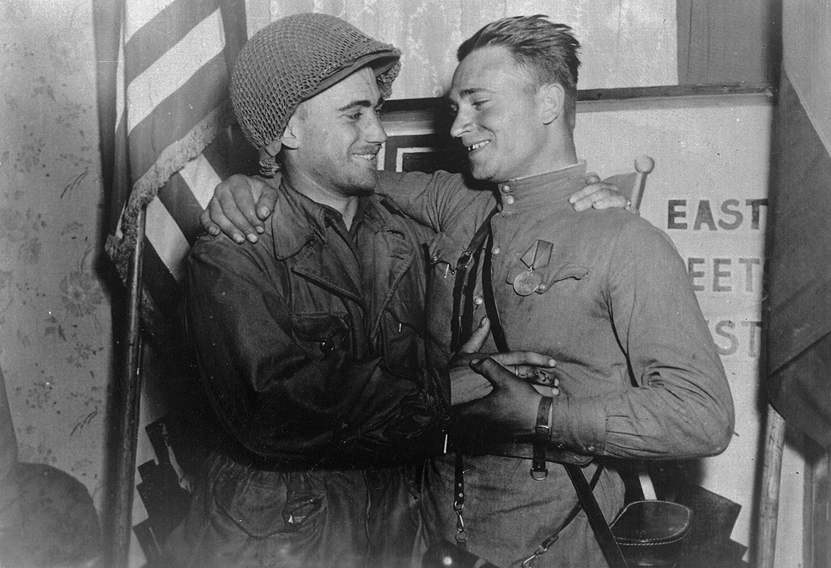 Happy 2nd Lt. William Robertson and Lt. Alexander Sylvashko, Red Army, shown in front of sign [East Meets West] symbolizing the historic meeting of the Soviet and American Armies, near Torgau, Germany on w:Elbe Day.