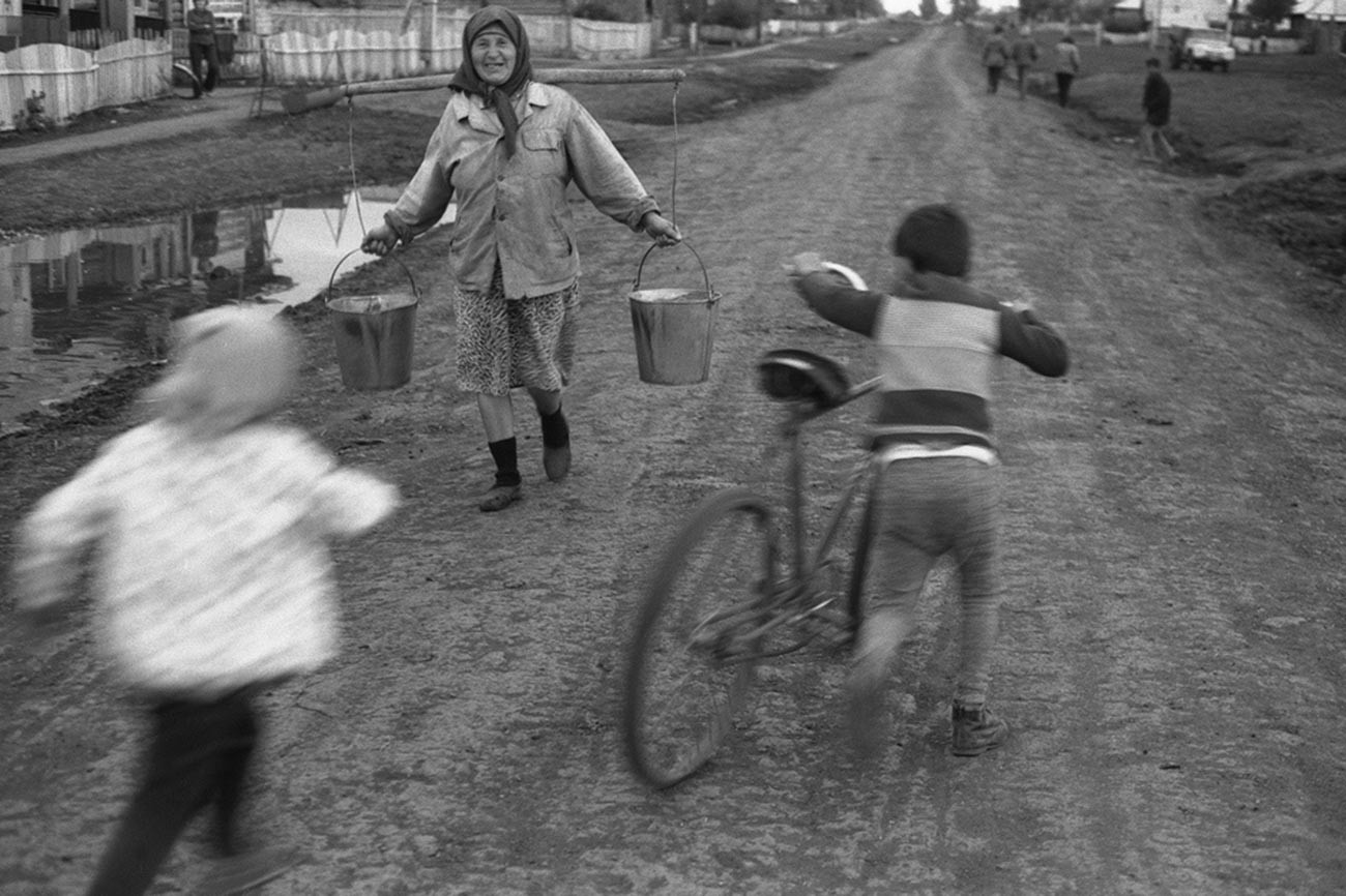 田舎道で自転車に乗る少年と天秤棒を持つ老女。1979年
