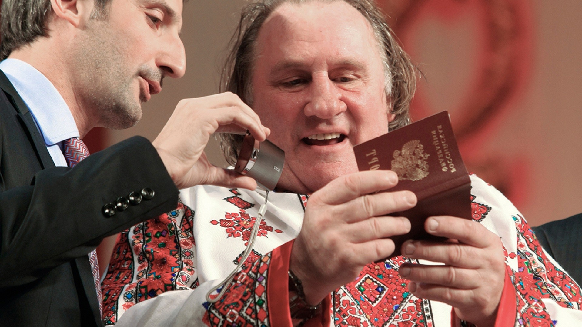Gérard Depardieu, désormais détenteur de la citoyenneté russe, en tenue traditionnelle mordve, examine son passeport avec son traducteur, sur la scène du Théâtre d'opéra et de ballet de Saransk, capitale de la République de Mordovie où il possède un logement.