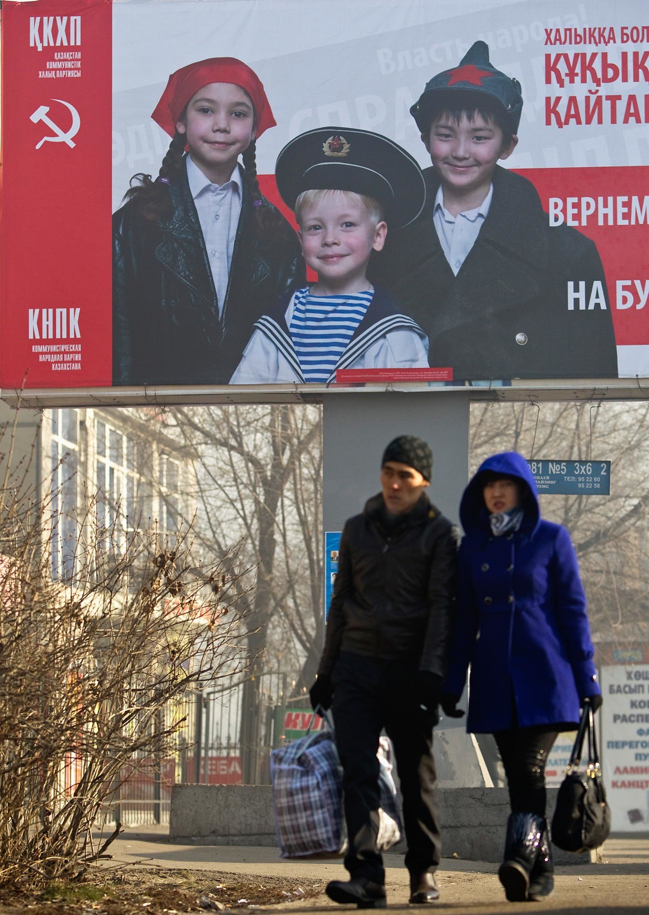 Orang-orang melewati poster pemilu Partai Rakyat Komunis Kazakhstan (QKHP) di Almaty.
