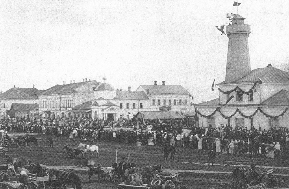 La Piazza del Commercio durante una festività. Sulla destra, la torre dei vigili del fuoco, costruita sul progetto dell'architetto A. M. Dostoevskij, fratello del celebre scrittore
