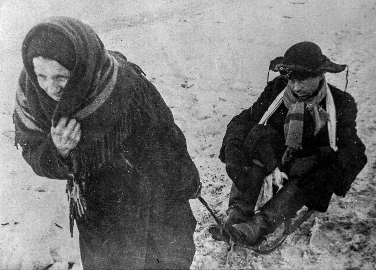 Блокада Лењинграда (8. септембар 1941. – 27 јануара 1944.). Жена вуче на санкама мужа исцрпљеног од глади. Велики отаџбински рат (1941-1945).