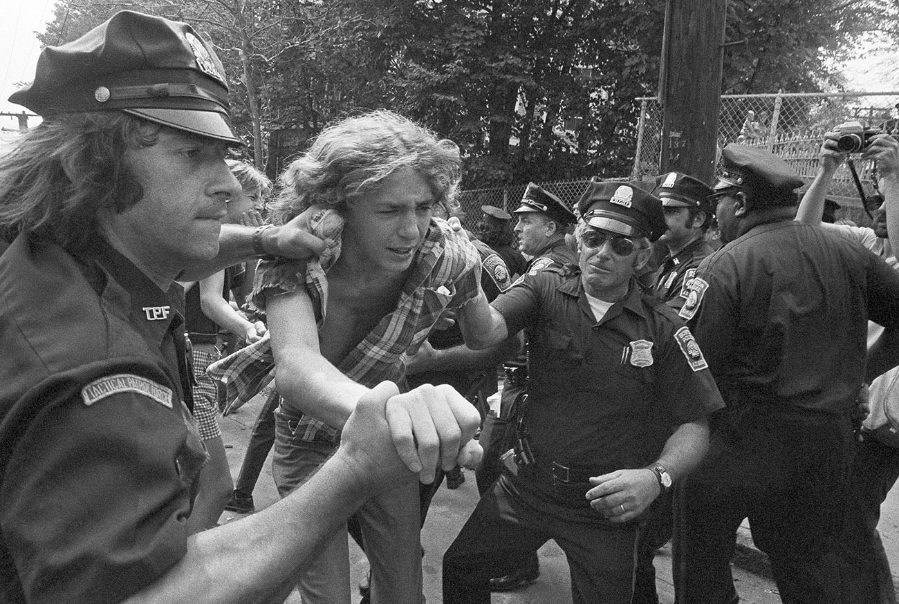 Младеж е задържан от полицията в Бостън пред гимназията на Южен Бостън , 13 септември 1974 г.
