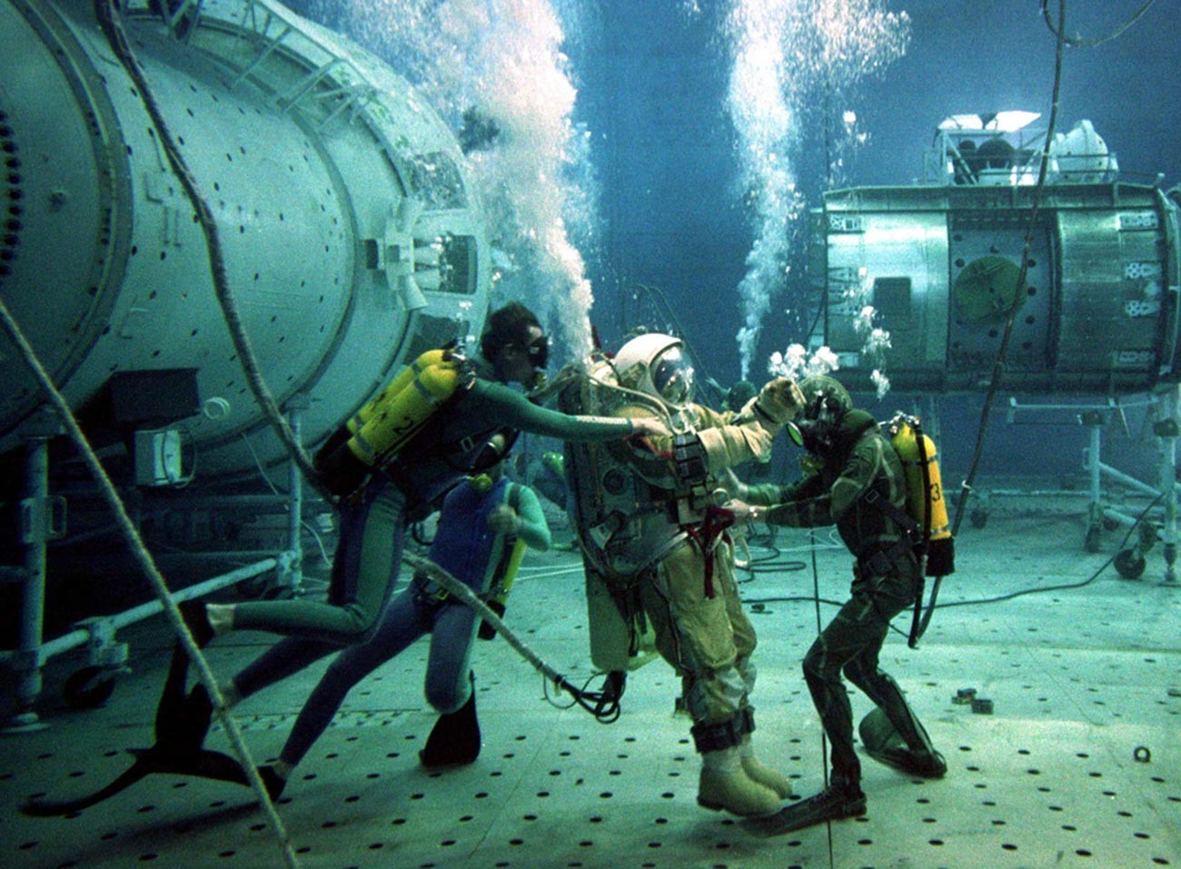 Instrutor de teste russo Oleg Puchkar é auxiliado por mergulhadores durante testes subaquáticos em uma réplica da estação espacial Mir danificada, em 4 de julho de 1997