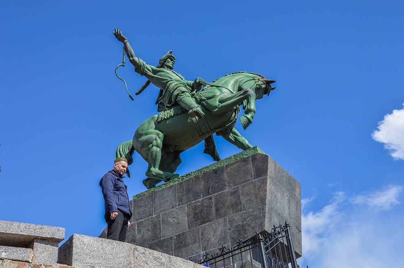 Seorang pria dengan topi khas Bashkir berfoto di dekat monumen Salavat Yulayev.