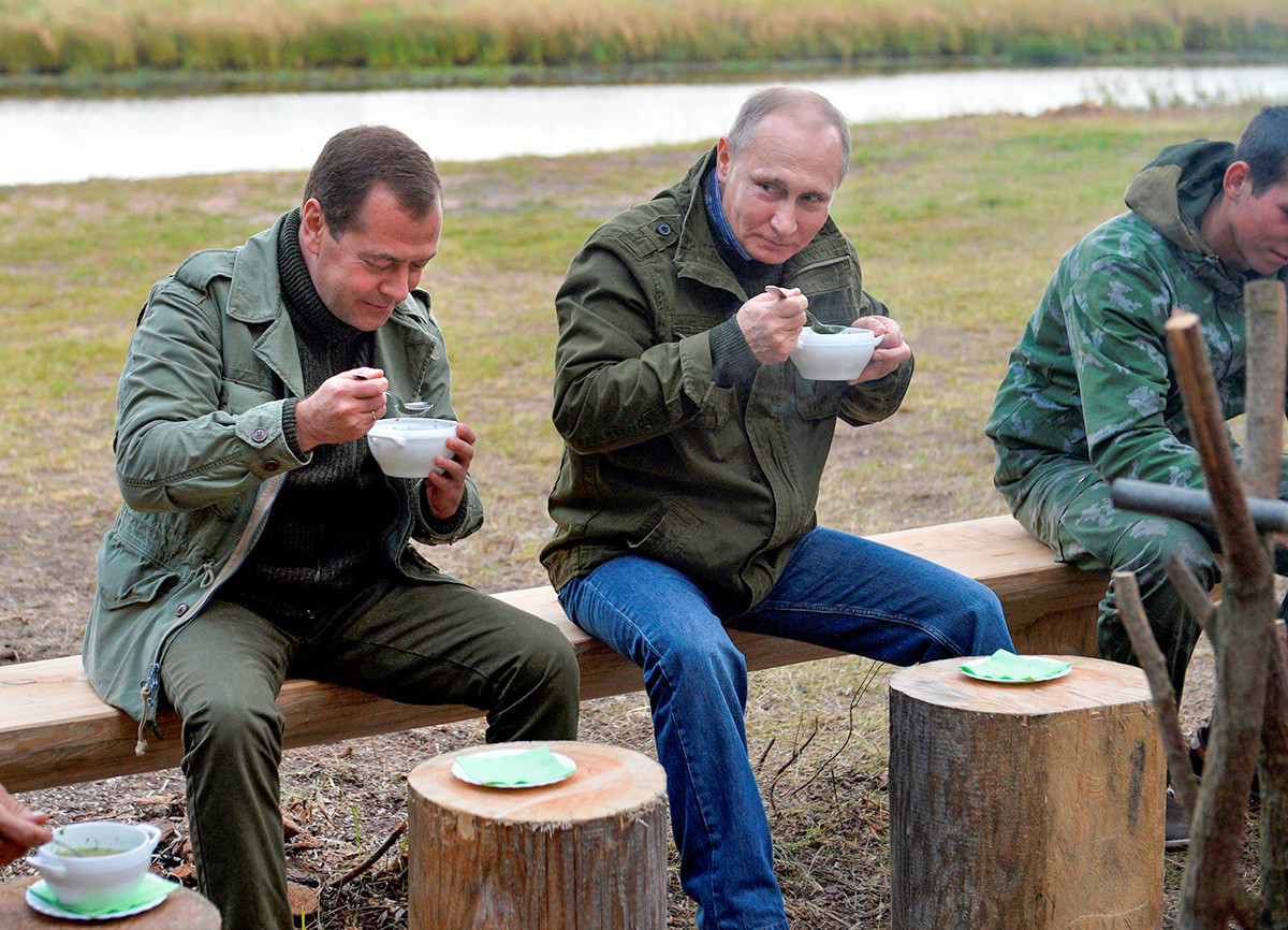 Russian President Vladimir Putin (C) and Prime Minister Dmitry Medvedev (C left) eat after touring on Lake Ilmen in Novgorod region, Russia, September 10, 2016
