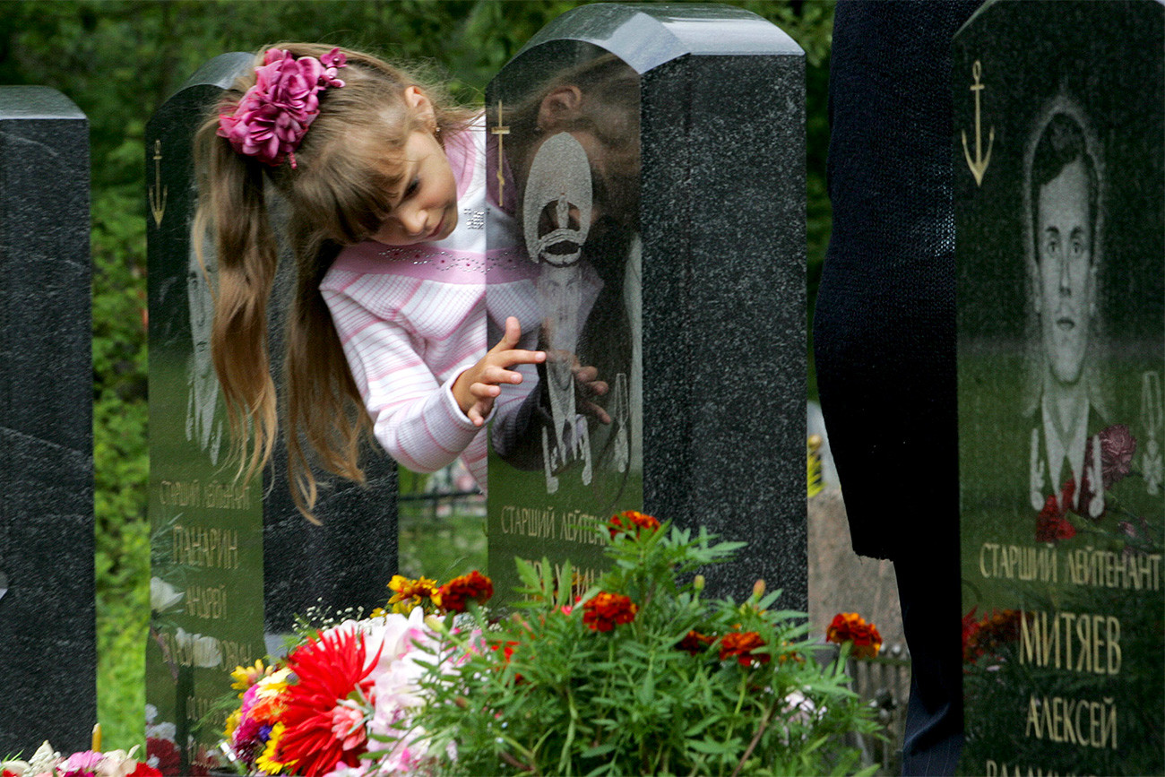 Kristina Yerakhtina, 7, menyentuh batu nisan ayahnya Sergei Yerakhtin, perwira kapal selam nuklir Kursk di pemakaman Serafimovskoye, Sankt Peterburg.