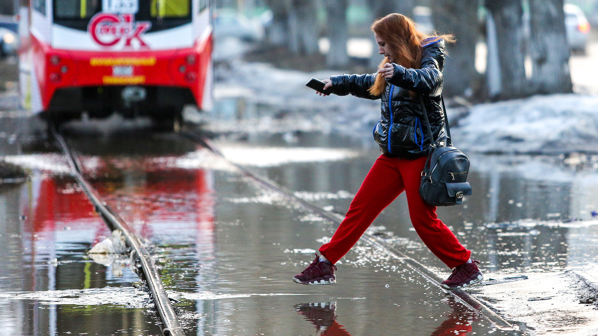 Omsk,Russia - April 7, 2021: A woman oversteps water in a flooded street. The flooding is caused by snowmelt