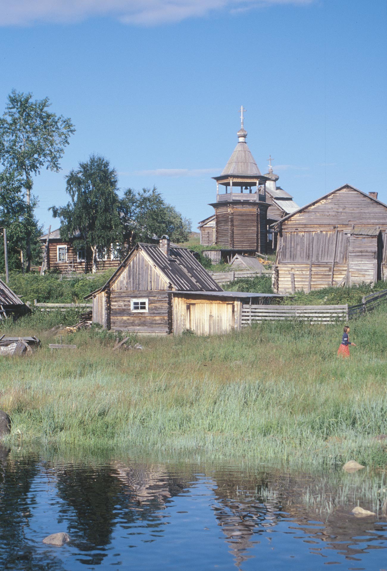 コヴダ村。丸太小屋と蒸し風呂と納屋。背景は聖ニコライ教会と鐘楼。2001年7月24日。