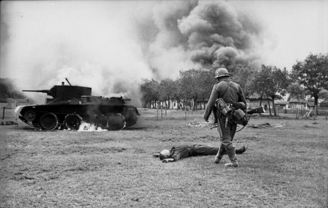 Soldat de l'infanterie allemande devant un conducteur de char soviétique tué et son char BT7 en flammes