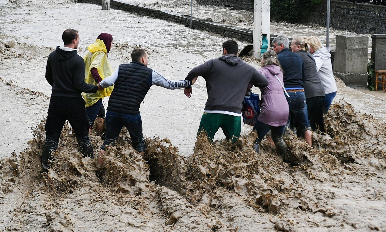 Луѓе си помагаат едни на други да поминат улица на Јалта. Крим го погодија обилни врнежи кои предизвикаа поплави.

