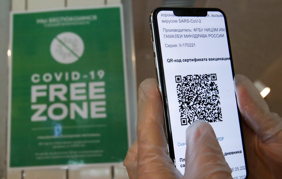 A person holds a mobile phone showing a QR code is seen at a 'COVID-19 free zone' sign at the entrance to the Mama Budet Rada restaurant for vaccinated customers in central Moscow. 