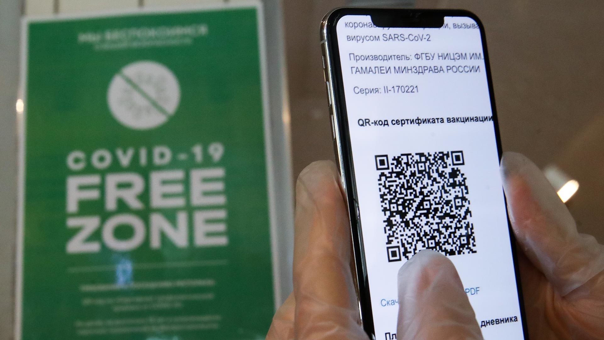 Seseorang memegang ponsel yang menunjukkan kode QR di dekat tanda “Zona Bebas COVID-19” di pintu masuk restoran Mama Budet Rada bagi pelanggan yang telah mendapatkan vaksinasi di pusat kota Moskow.