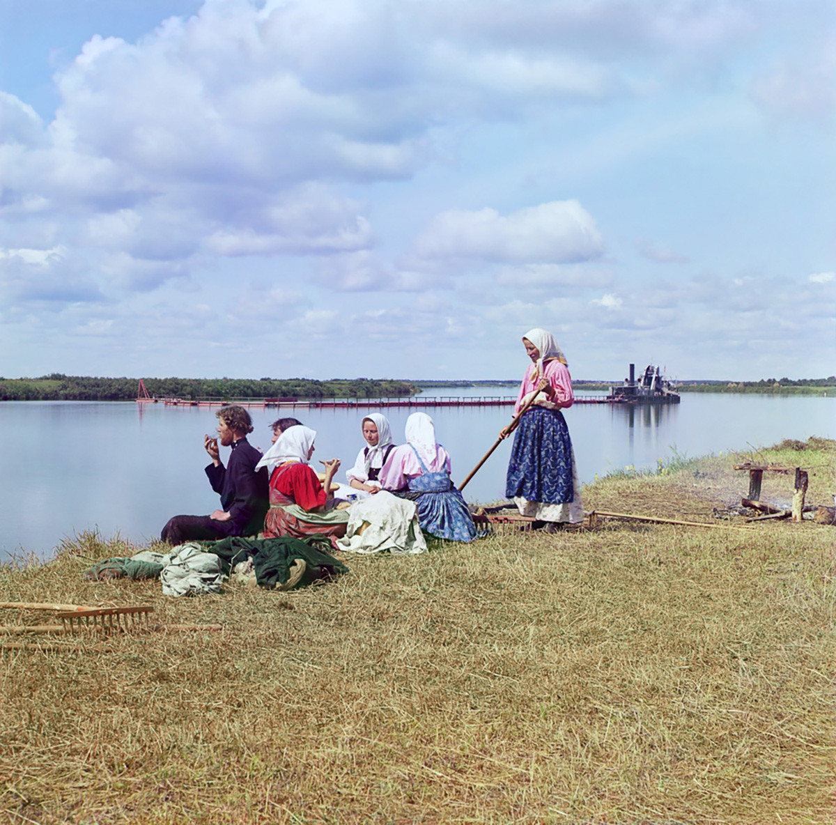 Cherepovets district. Peasants at tea break during hay gathering on island in Sheksna River. Background: dredging barge for navigation channel. Summer 1909