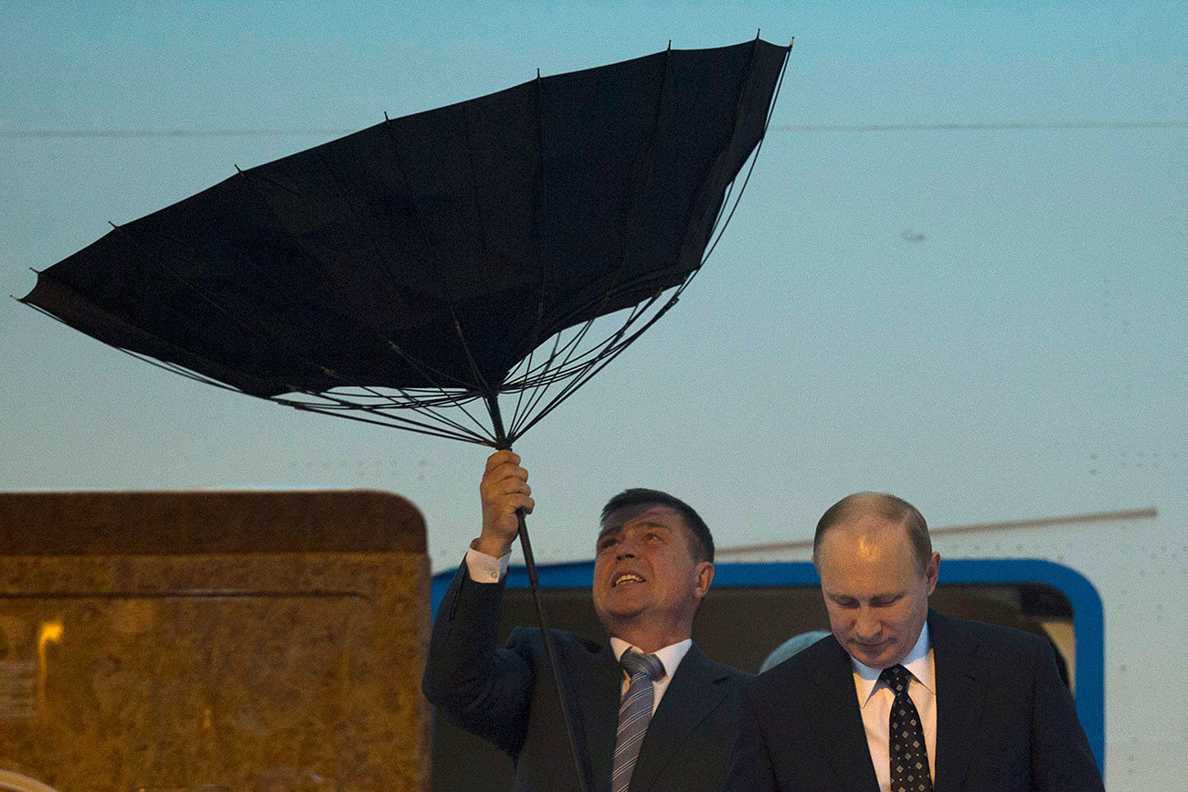 El personal de seguridad 'lucha' con un paraguas mientras el presidente ruso Putin sale de un avión a su llegada al aeropuerto, en 2014.