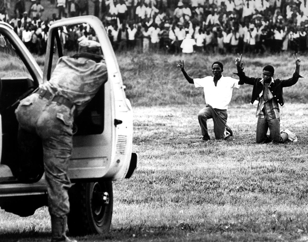 Mladi iz Soweta kleče ispred policije, držeći ruke u zraku pokazujući znak mira, 16. lipnja 1976., Soweto, Južna Afrika