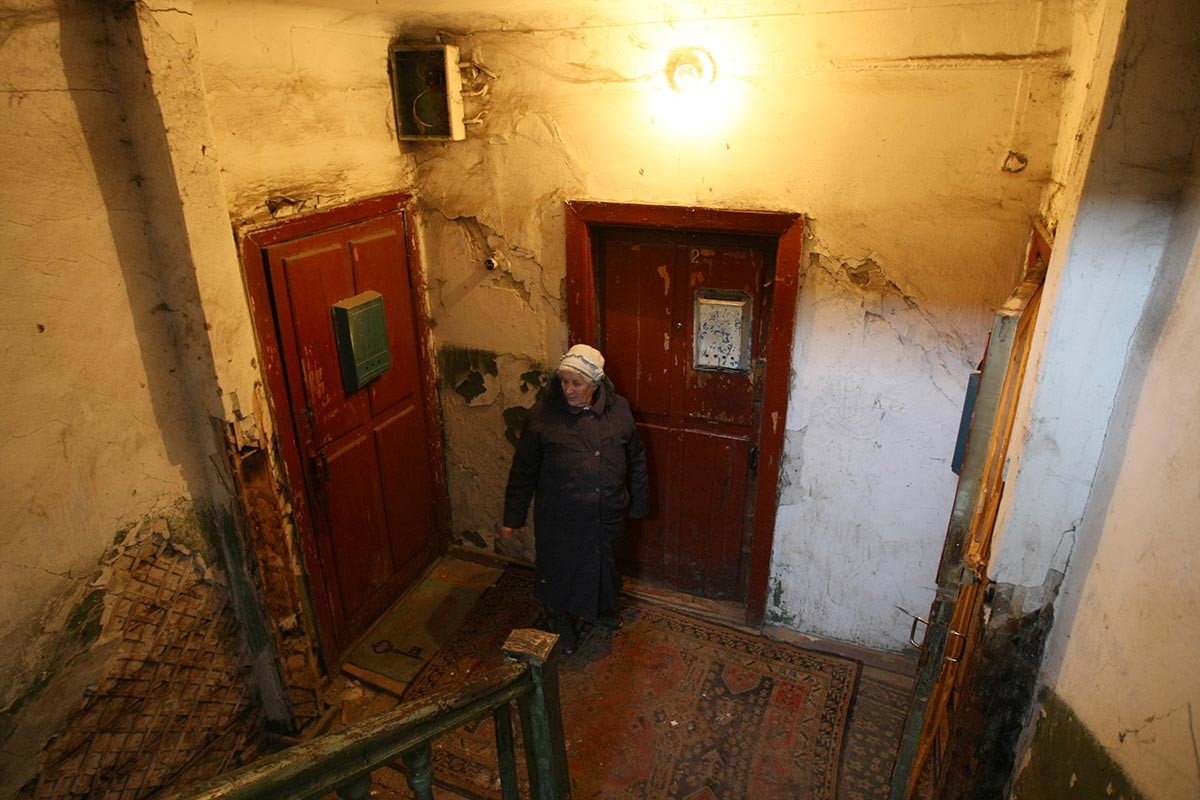 Жена стои на стълбището на жилищната си сграда в Новосибирск, Русия. Обърнете внимание на старите дървени врати