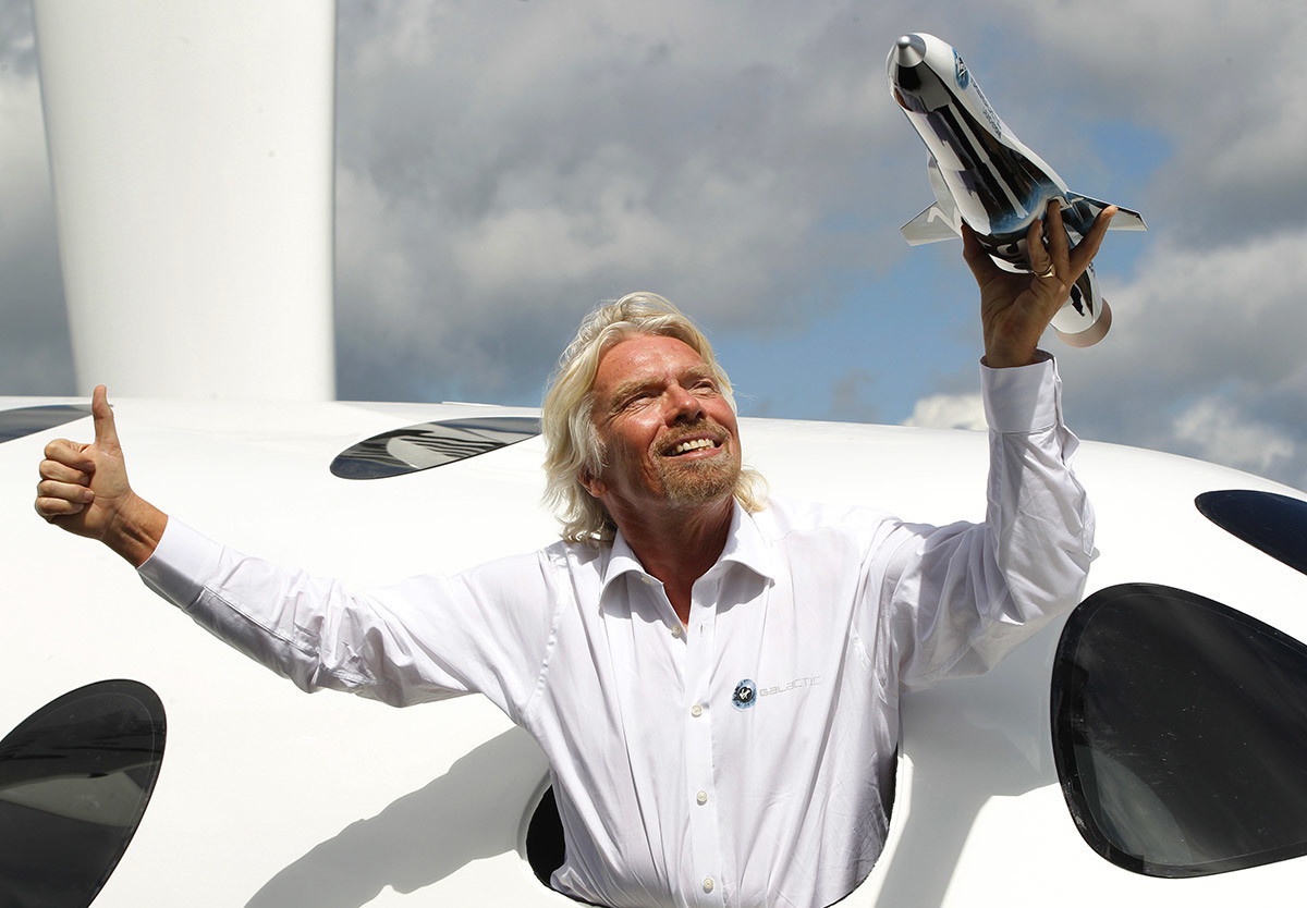 Richard Branson pozira kroz prozor replike svemirskog broda kompanije Virgin Galactic za koju kompanija kaže da će biti prva komercijalna svemirska linija na svijetu. Međunarodni zrakoplovni sajam u Farnboroughu, 11. srpnja 2012. Branson je također otkrio plan za lansiranje malih satelita u svemir.