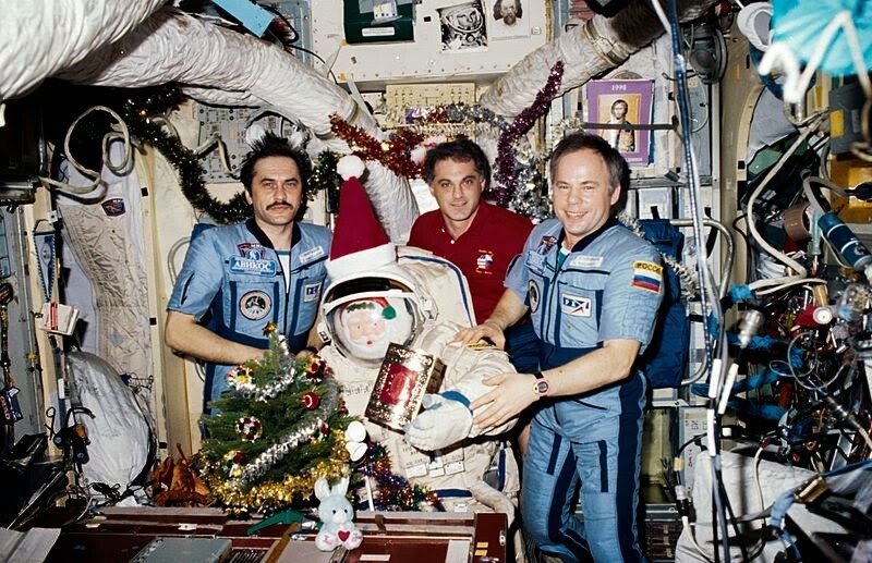 Weihnachten an Bord der Raumstation Mir während NASA 6. ViFlight-Ingenieur Pawel Winogradow, Missionsspezialist David Wolf und Kommandant Anatoly Solowyew posieren mit einer Weihnachtsmannpuppe in einem Orlan-Anzug, einem kleinen Baum, geschmückten Ästen und schwimmenden Geschenken.