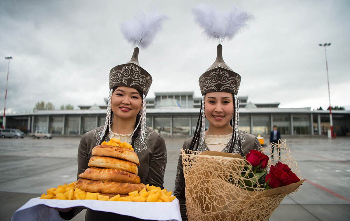 Zwei junge Frauen in traditioneller Tracht warten mit Blumen und Essen auf die Ankunft am Flughafen in Bischkek, Kirgisistan.