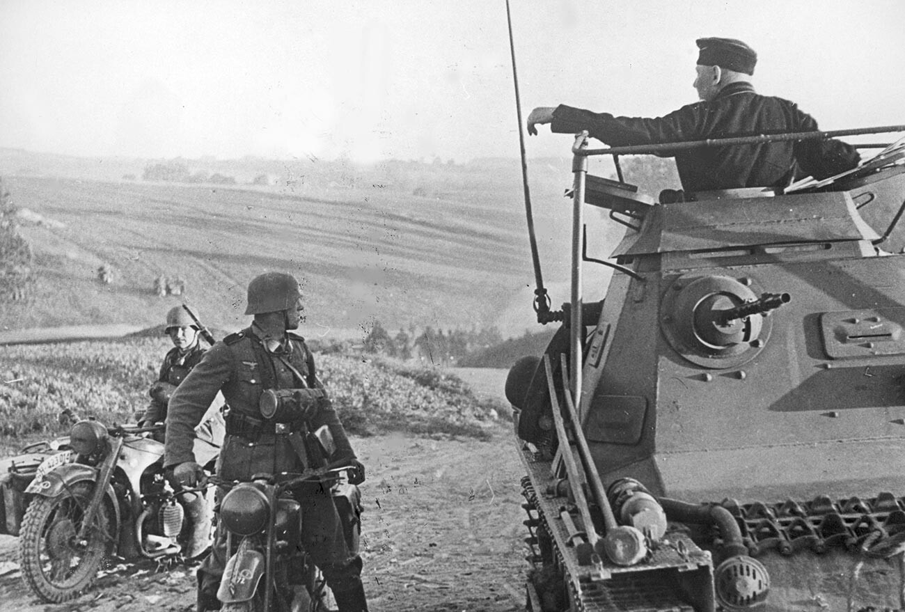 Двама мотоциклетисти на мотоциклети BMW R71 след завръщане от патрул докладват на командира си, застанал върху танк K1 PzBfWg тип 2 KI B