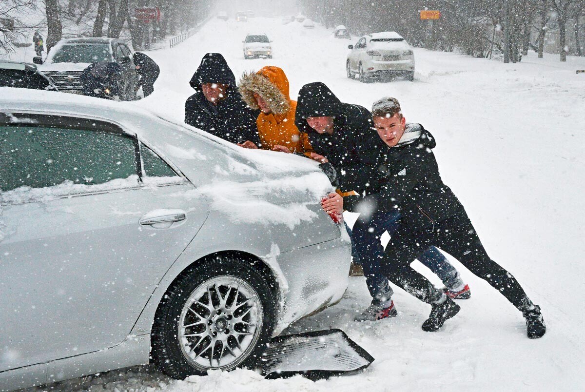 Homens empurram carro em Vladivostok, Rússia.