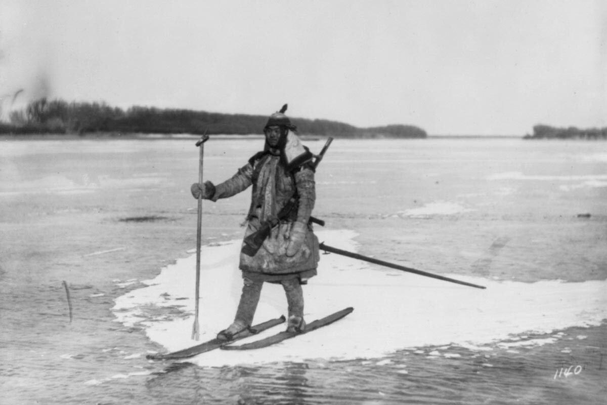 Seorang pemburu berski di atas gumpalan es yang terapung, dengan tombak dan senapan.