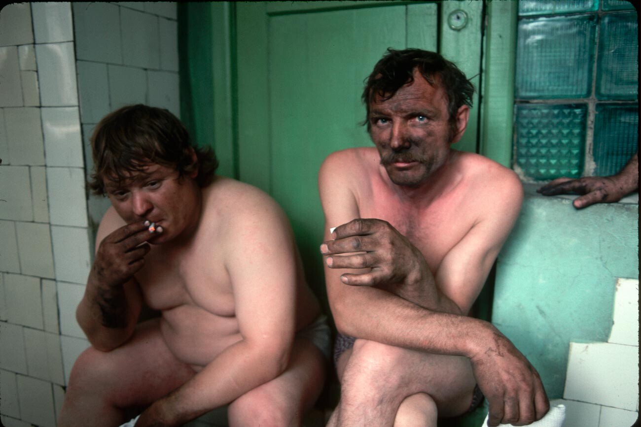 Two miners sit in a shower room after their shift. They live in a poor coal-mining and steel-manufacturing town enduring widespread economic hardships.