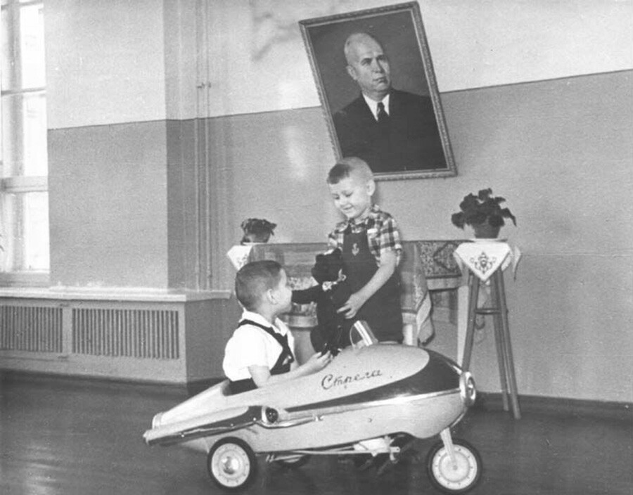 ソ連の幼稚園でかっこいい車のおもちゃで遊ぶ（ニキータ・フルシチョフの肖像画をバックに）