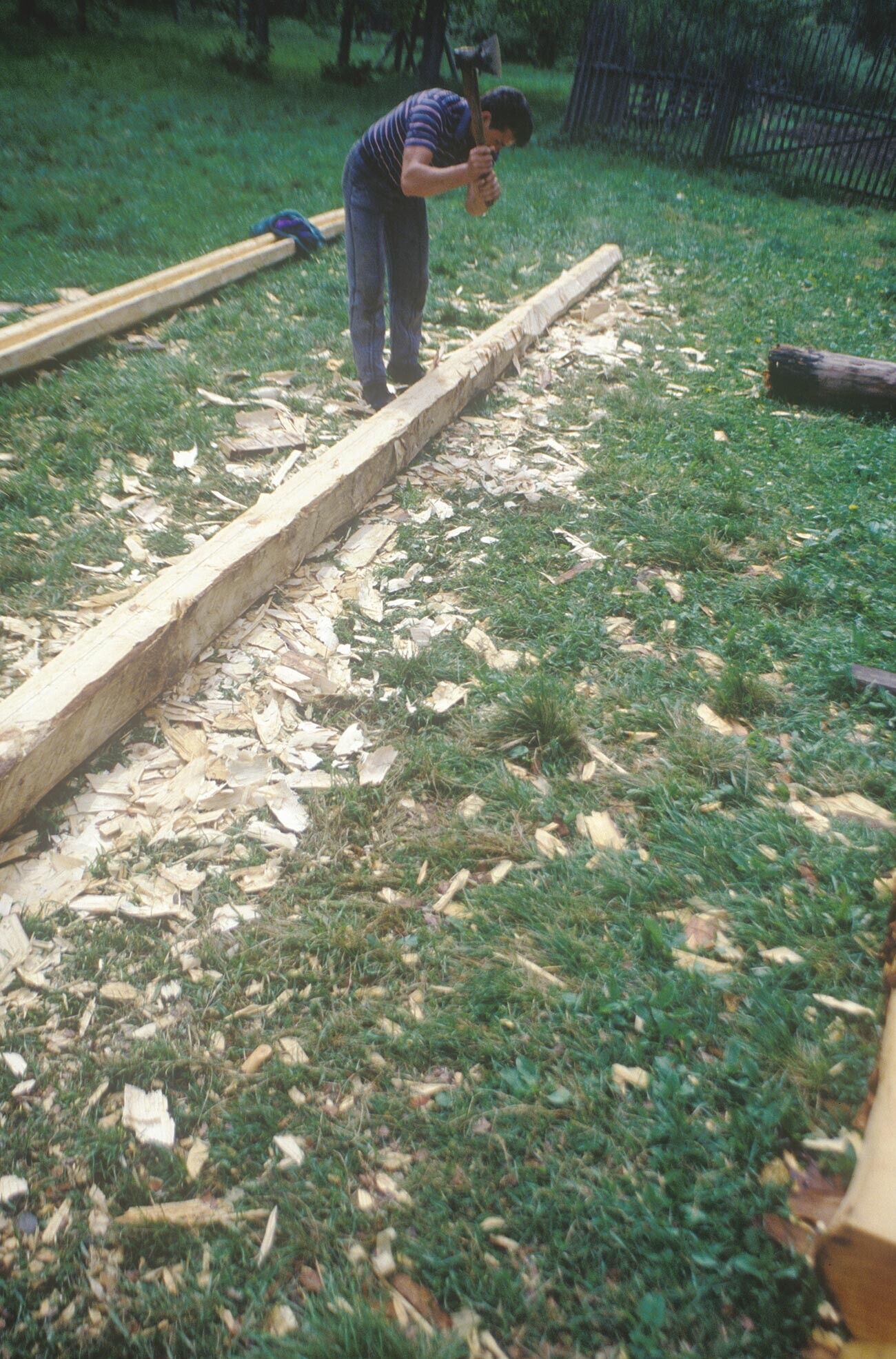 Vitoslávlitsi. Maestro carpintero trabajando en un tronco de pino. A su espalda, un canalón tallado con hacha y azuela a partir de un solo tronco. 27 de mayo de 1996