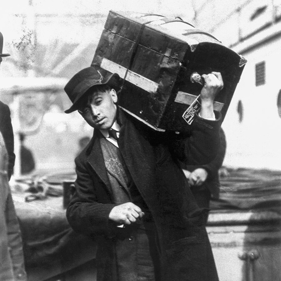 Mlad poljski priseljenec nosi prtljago na ladji President Grant na otoku Ellis Island v New Yorku leta 1907
