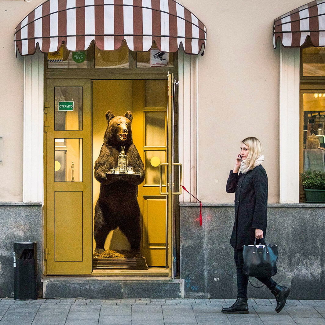 Ženska se v Moskvi sprehaja mimo trgovine z živili. Na vhodu je nagačen medved, ki ponuja vodko, 8. oktober leta 2018
