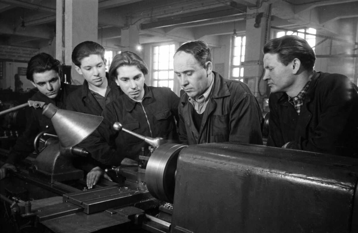 Seorang pekerja senior menunjukkan kepada karyawan cara kerja mesin bubut, 1952.