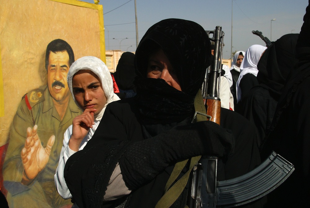 Perempuan Irak menggenggam senapan AK-47 di depan foto mantan Presiden Irak Saddam Hussein.