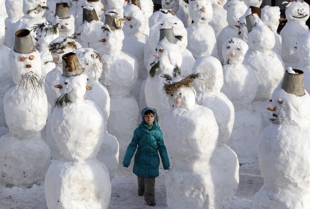 A girl walks among snowmen built as part of a display on a street in Moscow.