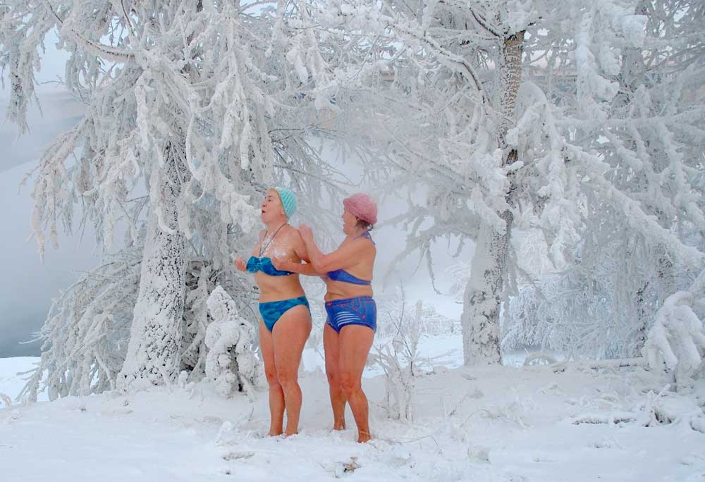 Seorang perempuan menggosok punggun perempuan lainnya dengan salju sambil berdiri di antara pohon yang diselimuti embun beku setelah mandi di Sungai Yenisey di Krasnoyarsk, Siberia. Para anggota klub mandi es setempat suka berenang di air es Sungai Senisey pada suhu sekitar -28 C.