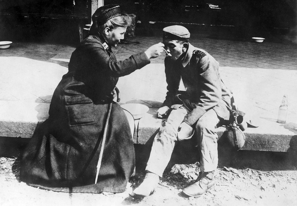 Une infirmière de la Croix Rouge française aide un mendiant, Allemagne, 1914-1918.
