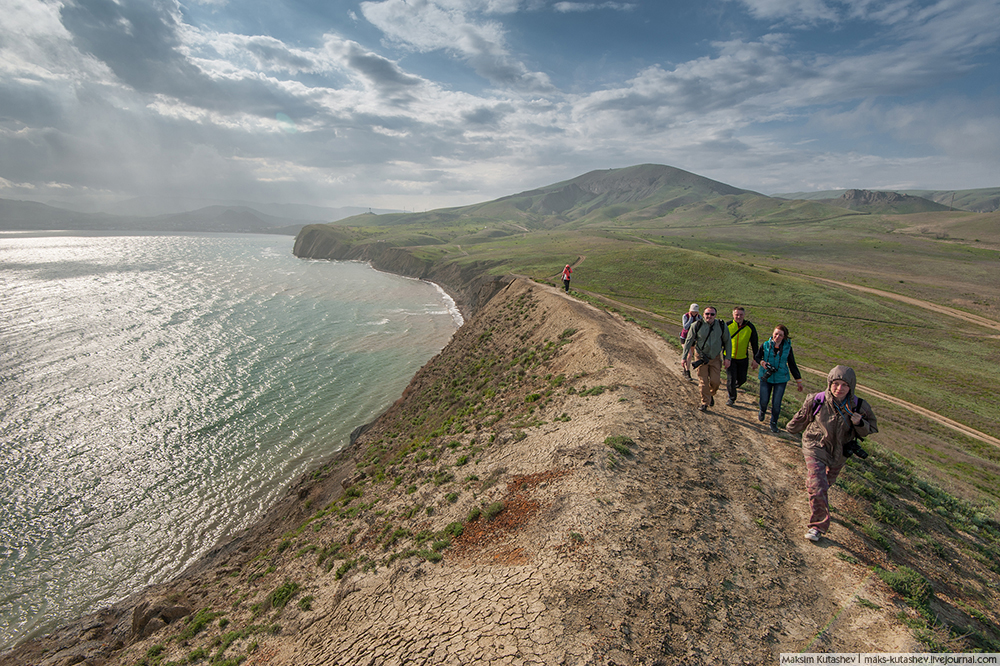Tikajski zaliv in rt Kameleon s turisti, ki se sprehajajo ob morski obali.