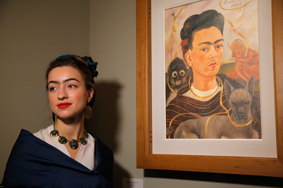 A visitor stylised as Frida Kahlo poses for photo next to a Frida's Kahlo self-portrait at the Frida Kahlo exhibition in St.Petersburg, Russia, Tuesday, Feb. 2, 2016. A retrospective exhibition of the renowned Mexican artist Frida Kahlo started on Tuesday at the Faberge Museum. This is the first Frida Kahlo exposition of such scale in Russia. The exhibition features 34 works, including paintings, drawings and lithographs