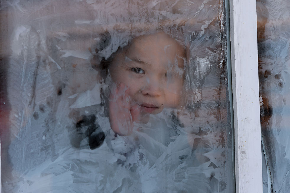 A girl looks through the window of the house on the winter range in Chumur-Oy, Tes-Khem district, Republic of Tuva.