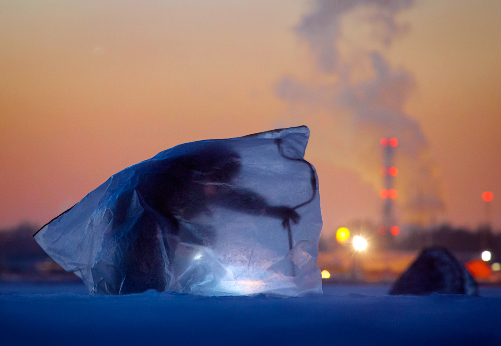 Заштићен најлоном од ветра и ниских температура, рибар буши лед на Неви. Фински залив, Санкт Петербург, Русија. 