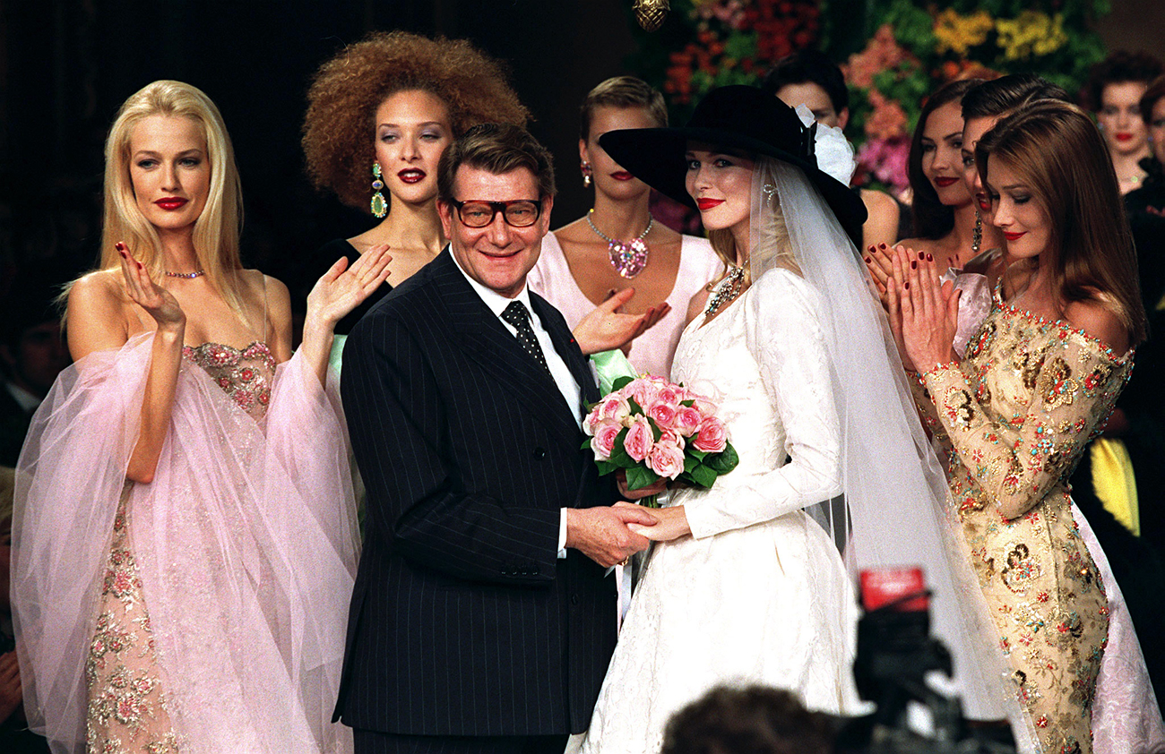 Францускиот моден дизајнер Ив Сен Лоран ја држи за раце германската манекенка Калудија Шифер додека холандската манекенка Карен Мулдер (лево), италијанската манекенка Карла Бруни (десно) и други модели во позадина аплаудираат по презентацијата на неговата модна колекција Есен/Зима 1996. 10 јули, 1996.