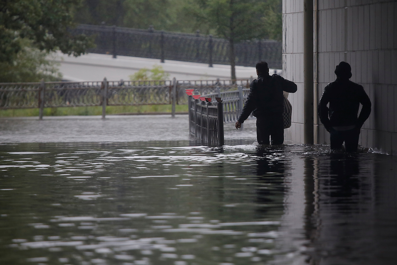 Dua orang pria berjalan menembus banjir selama hujan deras di kota Moskow, Rusia, 15 Agustus 2016. 