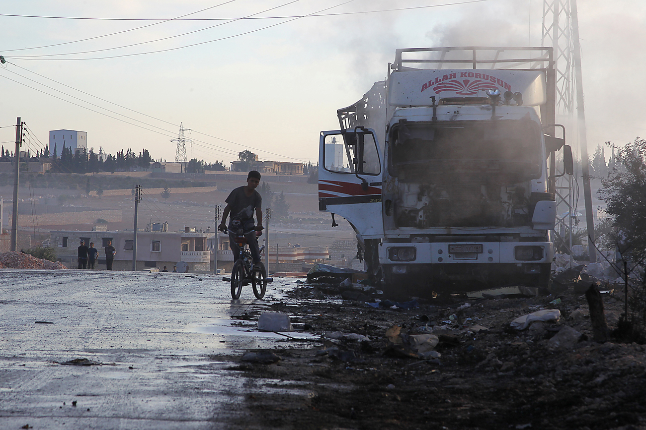 Ragazzo in sella a una bicicletta osserva un camion distrutto nella città di Urm al-Kubra, a ovest di Aleppo, in Siria. 