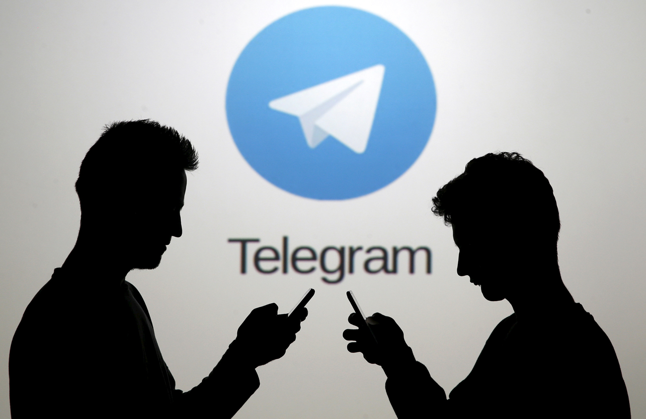 Due ragazzi posano con i loro smartphone davanti a uno schermo con il logo di Telegram.