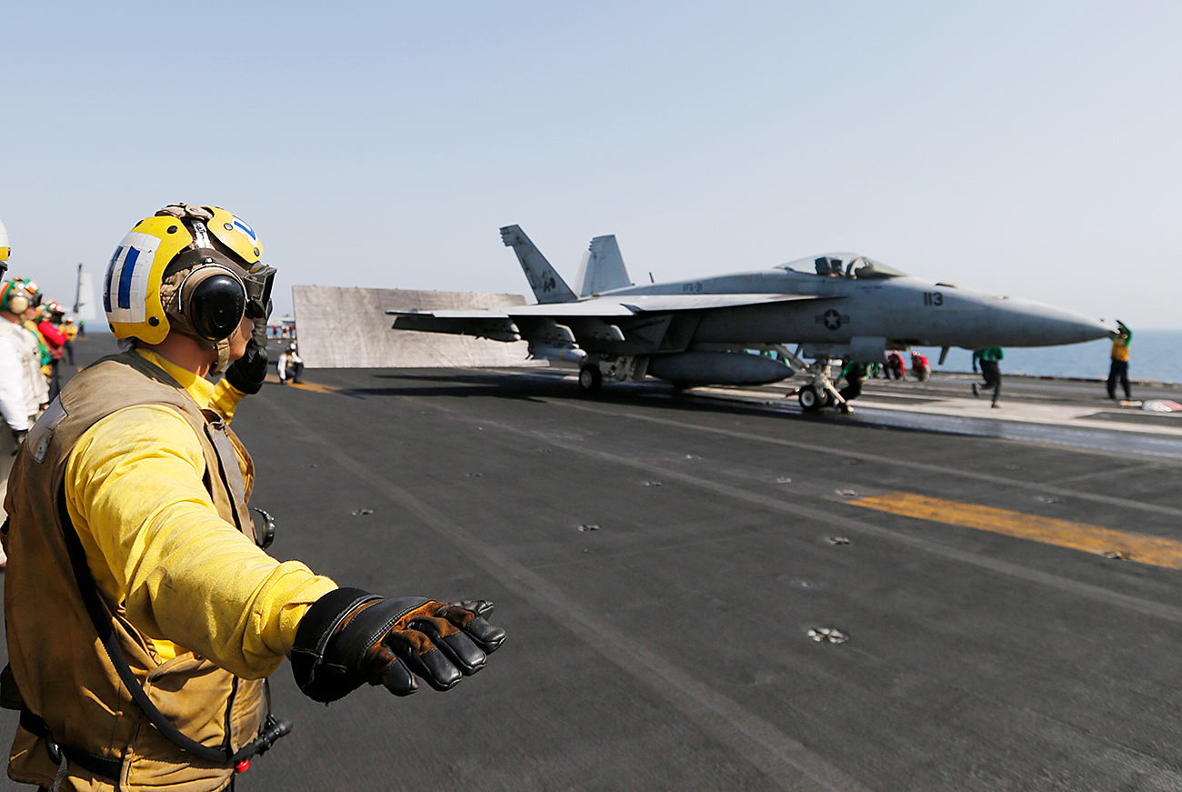 Flight deck crew member confirms the deck is all clear before a F/A-18C Hornet of Strike Fighter Squadron (VFA-87) take offs the aircraft carrier USS George H.W. Bush.