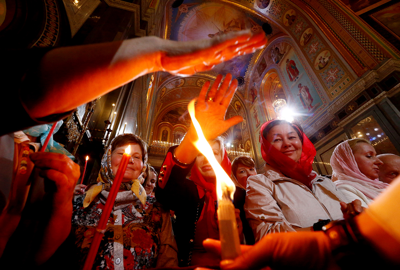 Worshippers reach out to touch candles with Holy Fire during an Orthodox Easter service at the Christ the Saviour Cathedral in Moscow, Russia