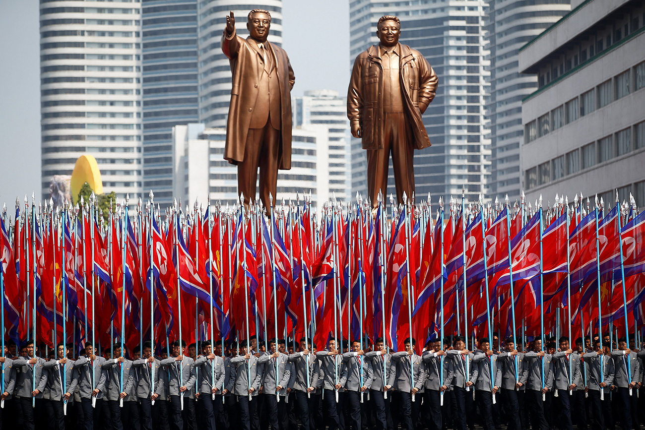Ljudi nose zastave Sjeverne Koreje ispred kipova Kim Il Sunga i Kim Jong Ila, na vojnoj paradi povodom 105. godina od rođenja Kim Il Sunga.
