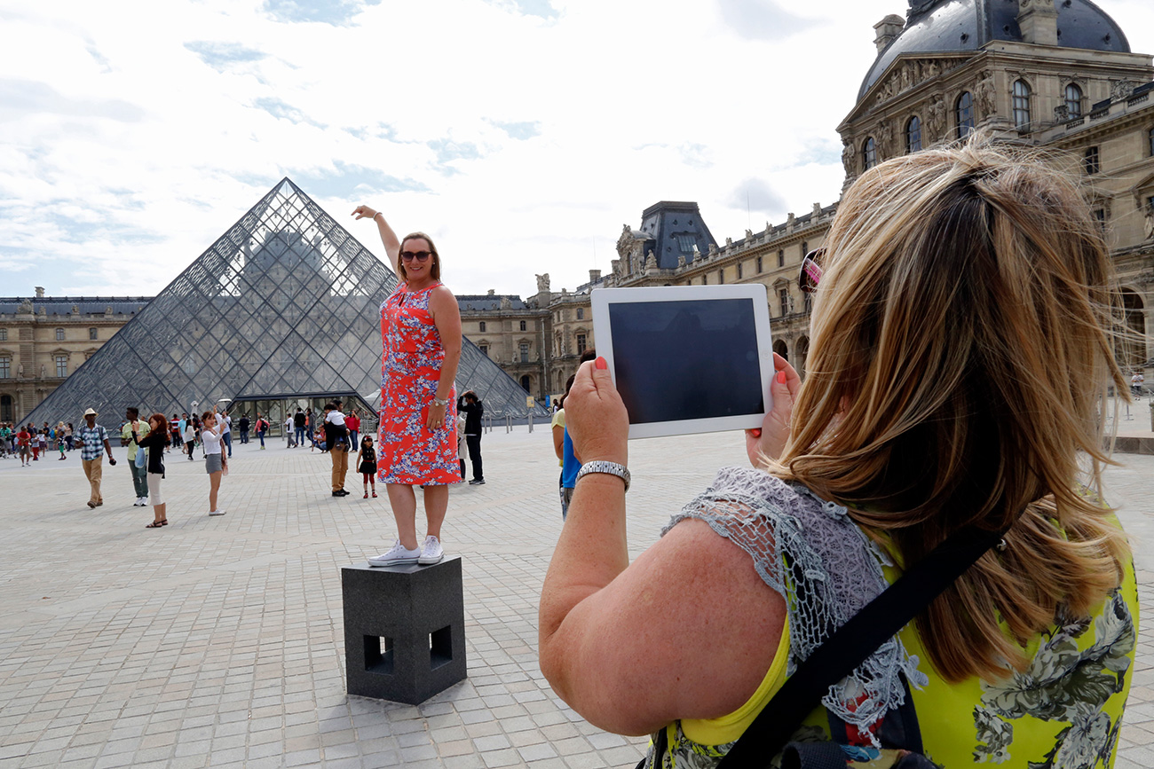 Ahead of the holiday season, the Russian MFA updated its recommendations on how not to offend the locals, how not to end up in jail, and how not to earn the reputation of a "bad Russian." Photo: A tourist poses for a souvenir picture near the Pyramid of the Louvre Museum in Paris.