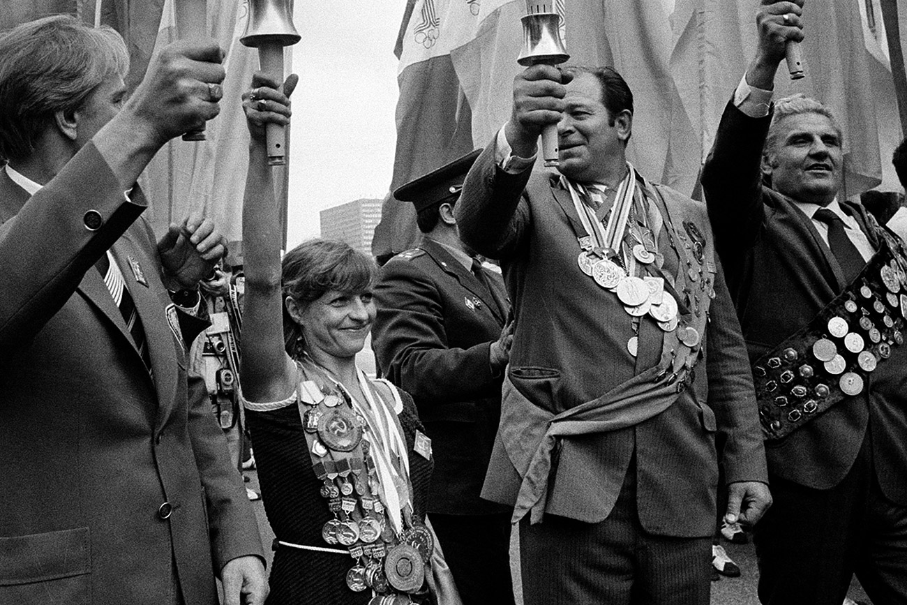 Holding a symbolic Olympic torch, former Soviet gold medalist Olga Korbut, center left, displays her many medals as she celebrates with others the arrival of the official Olympic Flame in Moscow, July 18, 1980. Opening ceremonies for the XXII Summer Olympics are scheduled for tomorrow. 